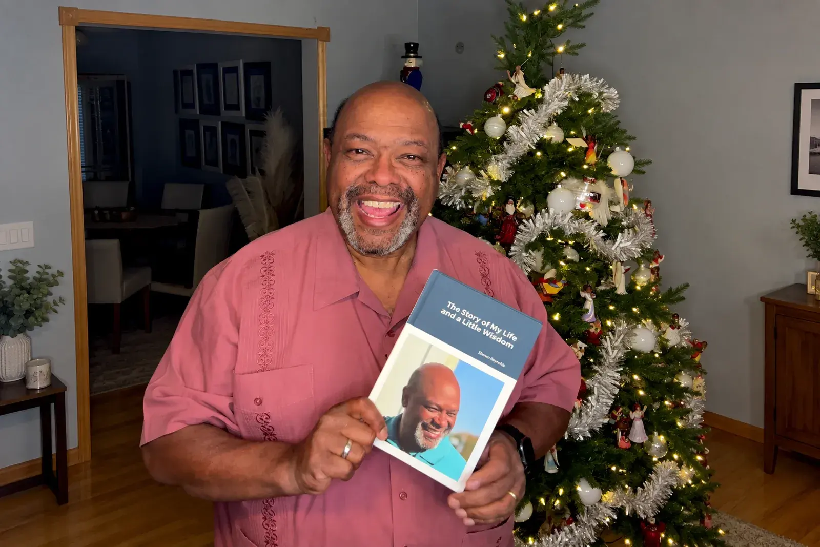 A man lovingly holds up his Kindred Tales hardcover memoir in front of a decorated Christmas tree
